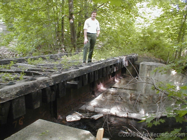 CRT bridge_oblique010514 Some improvements take major steps. In 2001, Cochituate State Park Supervisor Carey VandenAkker demonstrates the deteriorated deck of one of two railroad bridges just north of Old Connecticut Path. Creosoted timbers and crossties are heavy, and don't mix well with the trout in Cochituate Brook.